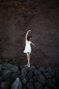 a girl in a white dress is standing on rocks